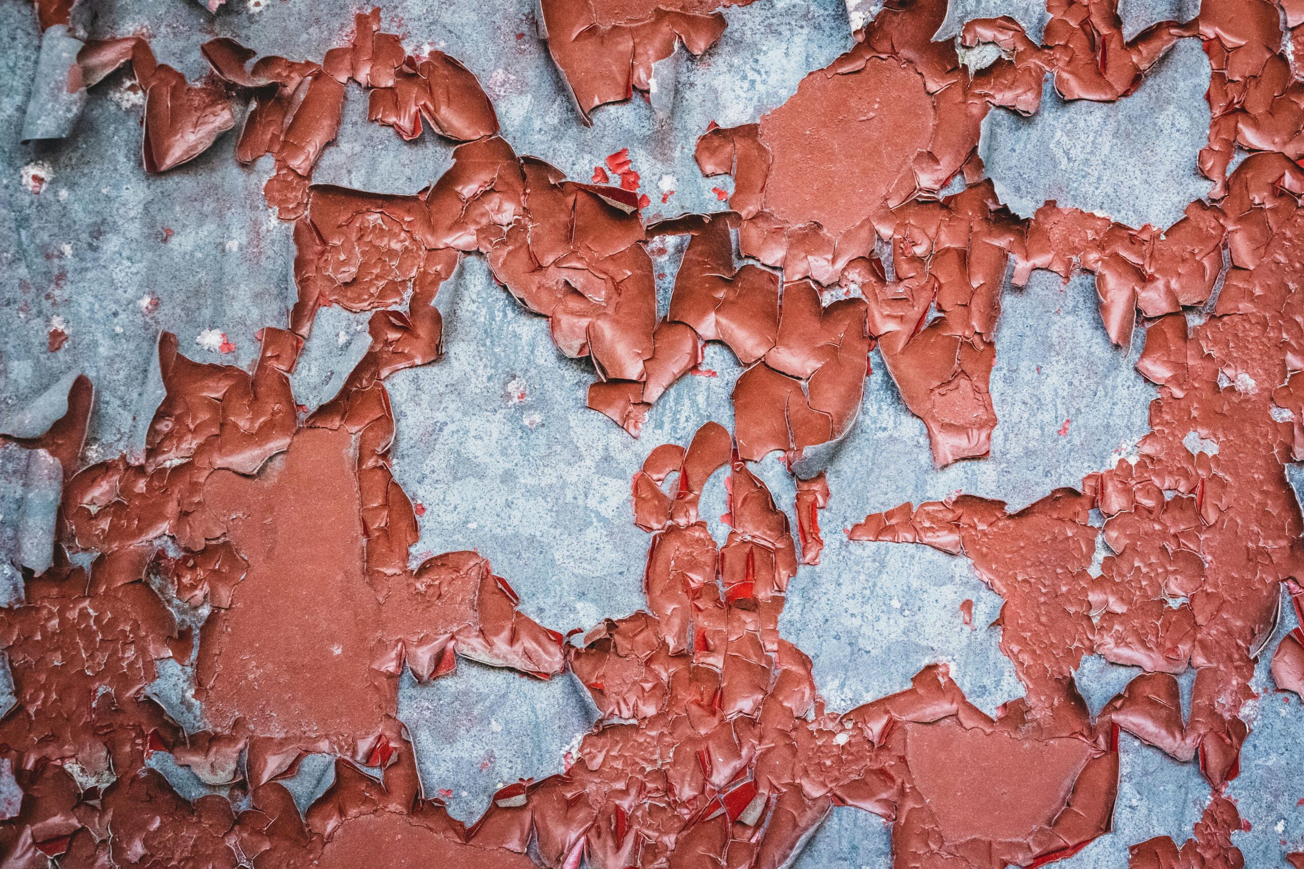Detailed close-up of a weathered and peeling painted wall texture in red and gray tones.