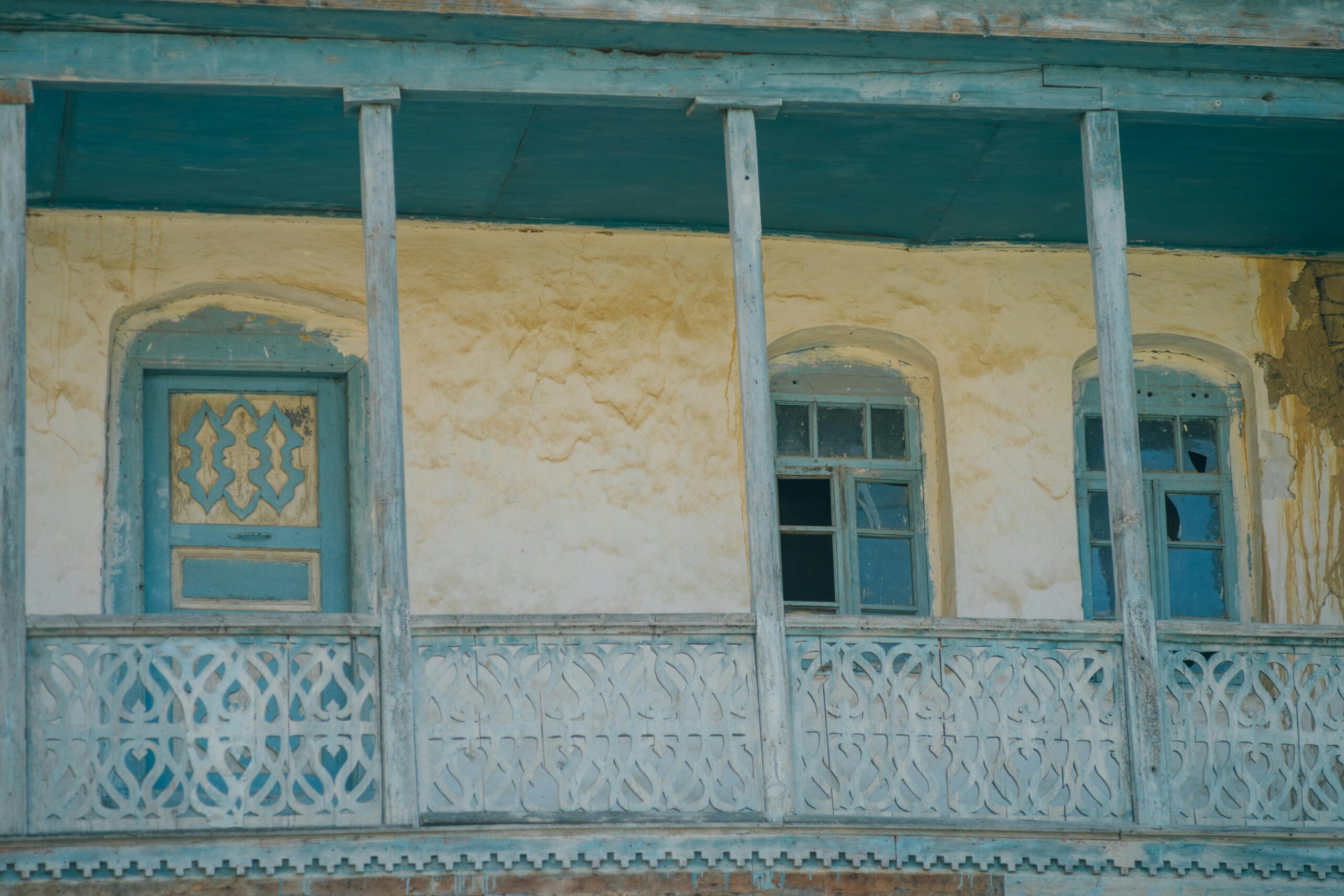 Close-up of a weathered traditional building facade with ornate designs and faded blue paint.